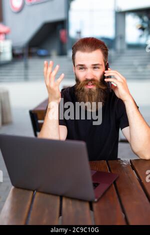 Happy male freelancer enjoying break for smartphone calling to best friend using roaming connection outdoors, cheerful bearded man making internationa Stock Photo