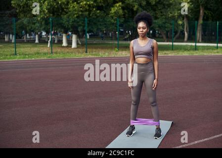 Woman during her fitness workout at outdoor with rubber resistance band. elastic for fitness on female legs. Train your legs. Training on a sports ground in the yard. Stock Photo