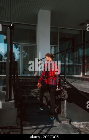 A handsome young bearded caucasian businessman with sunglasses in front of the company, holding an electric scooter in his hand Stock Photo