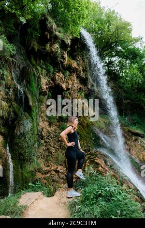 Young female nature explorer standing by the waterfall Stock Photo