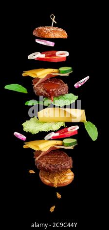 flying burger ingredients: cutlet, sesame seed bun, tomato, onion, green lettuce, cheese on black background, delicious double cheeseburger Stock Photo