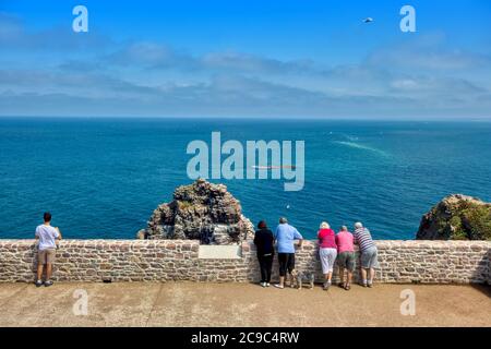 Cap Fréhel, Plévenon, Brittany, France. Tourists looking at the sea leaning against the wall of a panoramic terrace on a summer day. Stock Photo