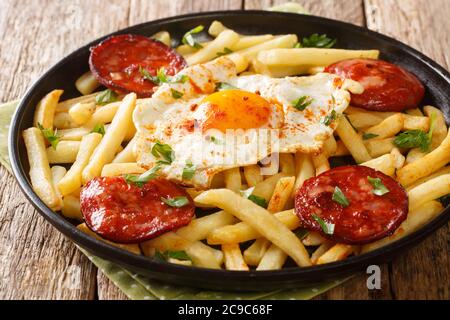 Huevos Rotos with fried potatoes and chorizo close-up in a plate on the table. Horizontal Stock Photo