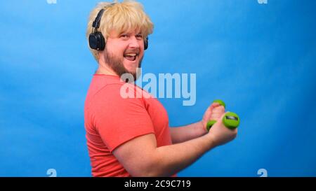 Funny fat man with dumbbells doing exercises on a blue background. Stock Photo