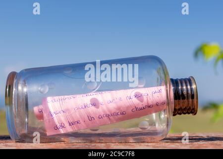 A handwritten letter on a pink sheet is rolled up inside a glass bottle Stock Photo