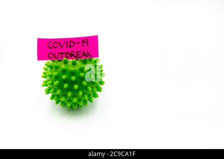 Closeup on green spiky ball as coronavirus representation and post-it note with Covid-19 Outbreak handwritten message isolated over white background, Stock Photo