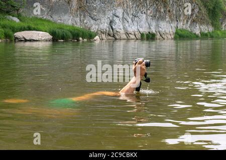 Man diving underwater holding camera in hand above water. Person swimming in natural water reservoir taking pictures with digital camera. Nature, wild Stock Photo