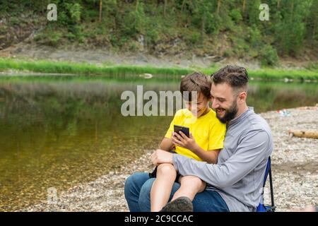 father and son using mobile phone and laughing. spending time on nature. Stock Photo