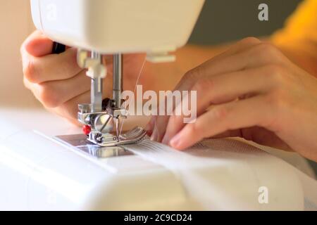 The process of sewing curtains from a mesh of white fabric. The rolled edge of the fabric is placed under the presser foot of the sewing machine. Close up view. Stock Photo