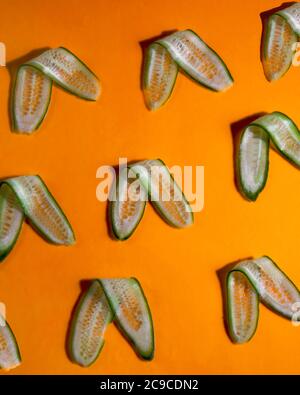 Long cucumber slices arranged on orange background Stock Photo
