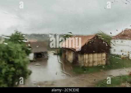 Drops on glass in rainy day. Rain outside window in autumn day. Texture of raindrops, wet glass. Rainy window background.Rural countryside. View throu Stock Photo