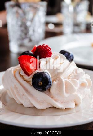 Meringue cake with berries on white plate with two empty crystal lemonade glasses on bokeh background. Stock Photo