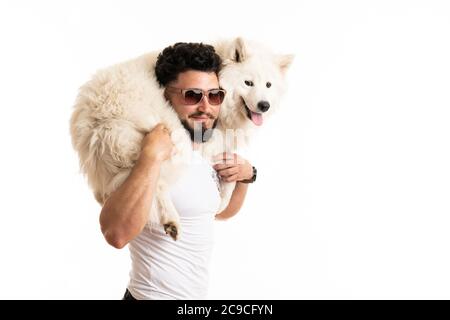 Stylish bearded man in glasses holds samoyed dog on his back, smiling and looking at the camera Stock Photo