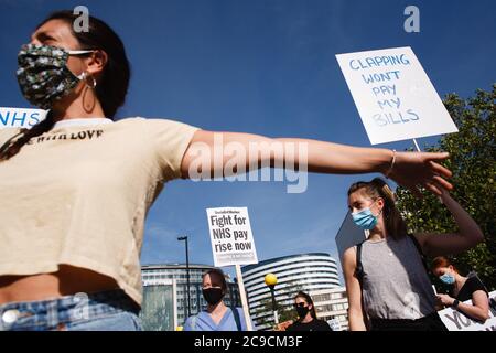 A woman activist outstretches her arms to maintain social distancing as the National Health Service (NHS) staff, protest their exclusion from a recently-announced public sector pay rise, demonstrate outside St Thomas' Hospital in London.Around 900,000 public sector workers across the UK are set to receive above-inflation pay rise this year as a gratitude gesture from the Treasury for their efforts during the coronavirus pandemic. The pay rise is however exclusive of nurses and other front-line staff owing to a three-year pay deal they negotiated in 2018 which led them to march in protest onto Stock Photo