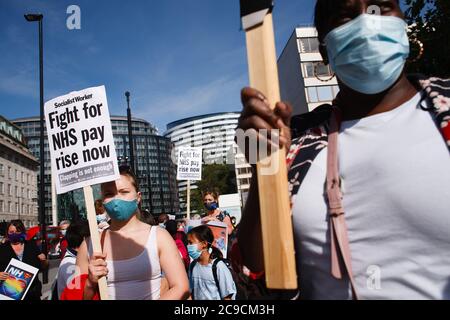 National Health Service (NHS) staff wearing masks are seen protesting their exclusion from a recently-announced public sector pay rise, demonstrate outside St Thomas' Hospital in London.Around 900,000 public sector workers across the UK are set to receive above-inflation pay rise this year as a gratitude gesture from the Treasury for their efforts during the coronavirus pandemic. The pay rise is however exclusive of nurses and other front-line staff owing to a three-year pay deal they negotiated in 2018 which led them to march in protest onto Parliament Street bound for Downing Street in Londo Stock Photo