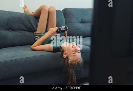 Happy little girl playing console game with wireless joystick. Stock Photo