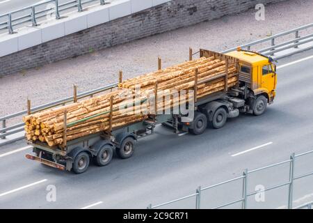 A timber truck drives along the city highway loaded with saw cut tree trunks Stock Photo