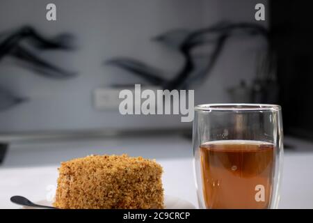 cup of tea in a double-botoom glass and piece of cake on white table in gray kitchen. High quality photo Stock Photo