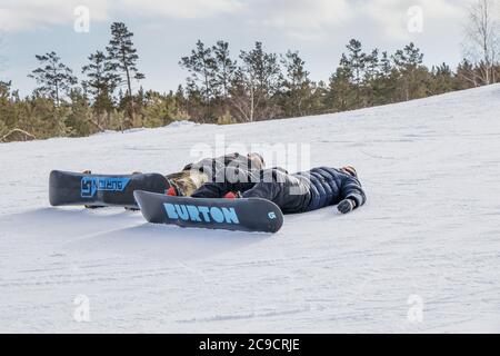 Yekaterinburg, Russia - February 26, 2019. Two young guys in the snowboards lie on the ski slope and relax. Stock Photo