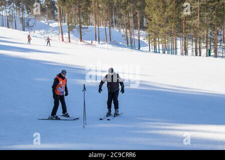 Yekaterinburg, Russia - February 26, 2019. Training slope of the sports complex on Uktus Mountain. A elder trainer teaches a man skiing. Stock Photo