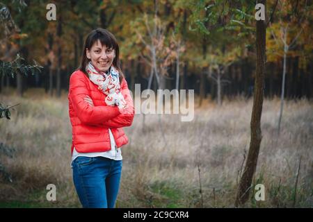 Beautiful young smiling woman in jeans and bright jacket outdoors in autumn forest Stock Photo