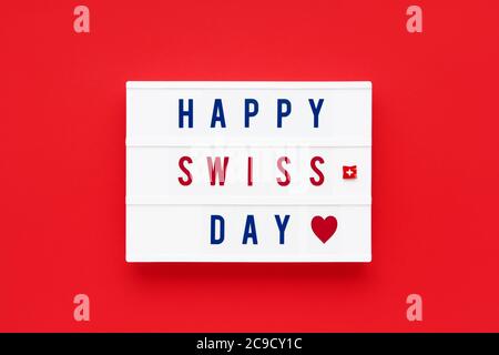 HAPPY SWISS DAY written in a lightbox on a red background. Independence day date. Top view. Stock Photo