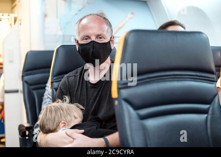Man in the mask holding his small sleeping son in the airplane Stock Photo