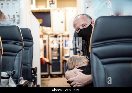 Man in the mask holding his small sleeping son in the airplane Stock Photo
