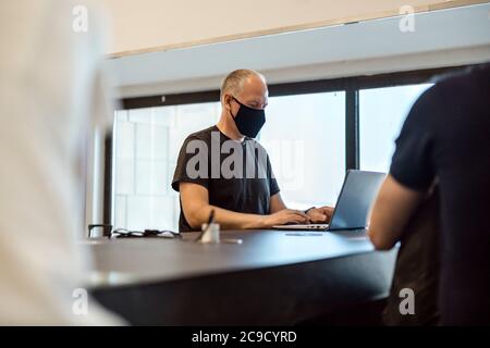 Man in a mask working at his laptop at the airport waiting for his flight Stock Photo