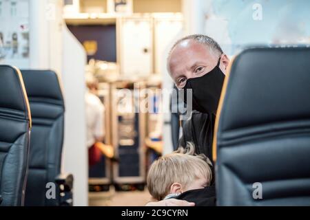 Man in the mask holding his small sleeping son in the airplane Stock Photo