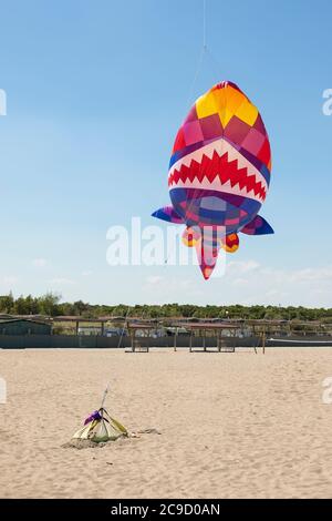 Big, colorful shark kite flying over the beach of camping Vittoria, Rosolina Mare, Veneto, Italy. Vertical shot. Stock Photo