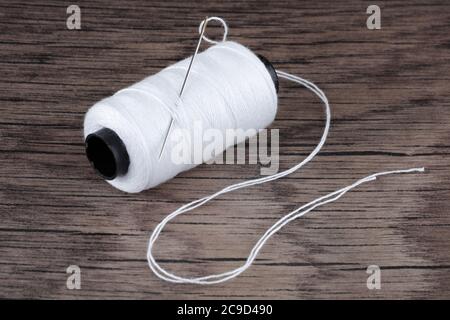 reel of white cotton and needle on wood Stock Photo