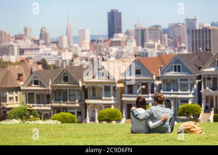 San Francisco tourist attraction at Alamo Square, the Painted Ladies famous postcard row, California travel. Couple tourists relaxing in grass Stock Photo
