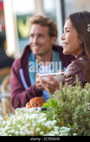 Happy people eating brunch at cafe. Young couple hipsters drinking coffee at restaurant table outside sidewalk terrace at parisian bistro in european Stock Photo