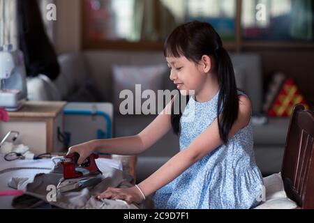 Asian little girl sitting and ironing in the house with smile and happy Stock Photo