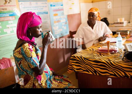 A nurse distributes malaria prophylaxis specialized for pregnant women to a female patient at a health center in Kouroussa, Guinea, West Africa. Stock Photo