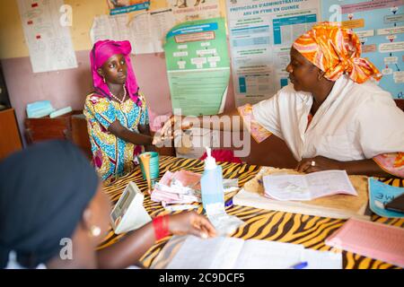 A nurse distributes malaria prophylaxis specialized for pregnant women to a female patient at a health center in Kouroussa, Guinea, West Africa. Stock Photo