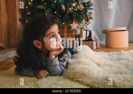 Christmas portrait of beautiful little girl lying on floor under the christmas tree. Winter holiday Xmas and New Year concept Stock Photo