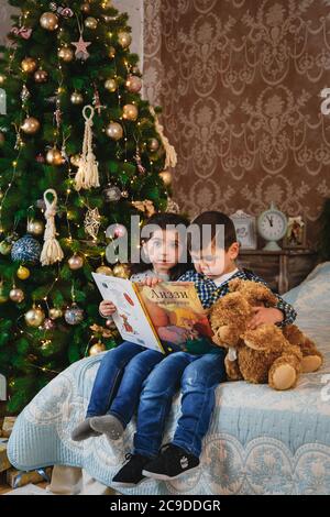 Christmas portrait of small kids sitting on bed with presents under the christmas tree. Winter holiday Xmas and New Year concept Stock Photo