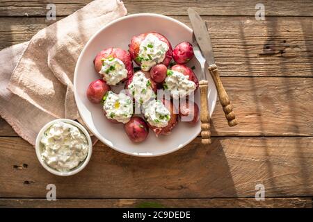 Young, boiled potatoes with sour cream and green onion on a wooden background Stock Photo