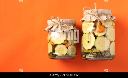 Pickled patissons and cucumbers in glass jars on a bright orange background, Top view, Copy space Stock Photo
