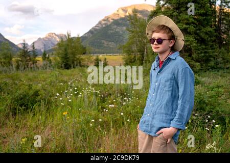 Teenager Traveler wearing hat and sunglasses, staying relaxed outdoor with rocky mountains on background. Summer vacation concept. Stock Photo