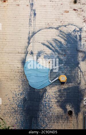 “Girl with a pierced eardrum” with added medical face mask covering during the Covid 19 pandemic. Banksy graffiti artists work on Hanover Place, in Br Stock Photo