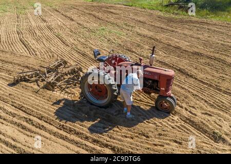 Otsego, Michigan - A 90-year-old farmer does an on-field repair to a Farmall Model M tractor, while disking a field on a small farm in western Michiga Stock Photo