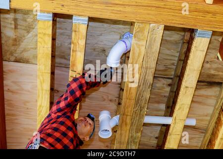 PVC plastic sewer toilet white pipe in the plumber gluing, on wooden frame ceiling beam of house Stock Photo