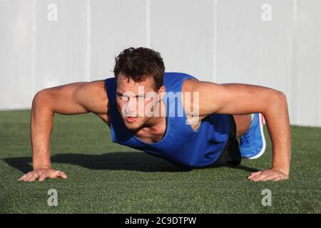 Push ups - fitness man exercising outside doing pushups. Male fitness instructor doing Push Ups on stadium grass at outdoor gym center. Stock Photo
