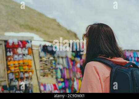Female traveler on market in mountainous terrain. Woman tourist considering souvenirs in shopping booths. Stock Photo