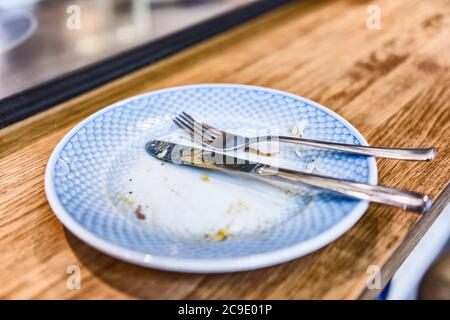 Empty plate after finished meal at restaurant - fork and knife resting on done dinner with crumbs at bistro counter. Stock Photo
