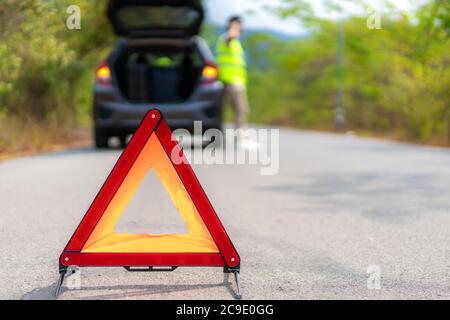 Breakdown triangle sign on road with worried Asian man talking by mobile phone with insurance or car service center company after car breakdown on cou Stock Photo