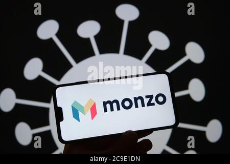 Stone / United Kingdom - July 30 2020: silhouette of smartphone with Monzo bank logo on the screen and COVID-19 shape on the blurred background. Monzo